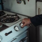 gastroback - Close-up of a hand turning a knob on a retro gas stove in a home kitchen setting.