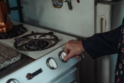 gastroback - Close-up of a hand turning a knob on a retro gas stove in a home kitchen setting.