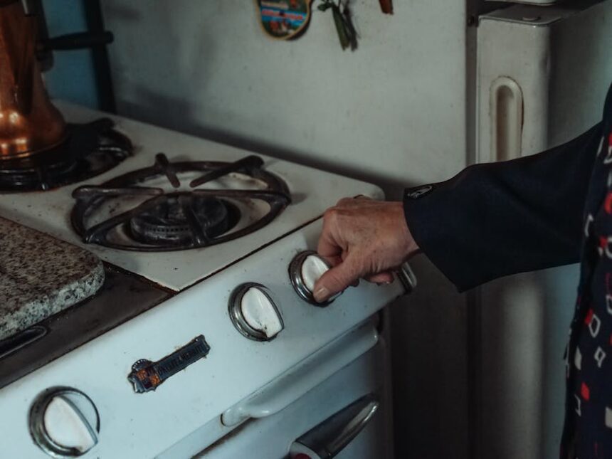 gastroback - Close-up of a hand turning a knob on a retro gas stove in a home kitchen setting.