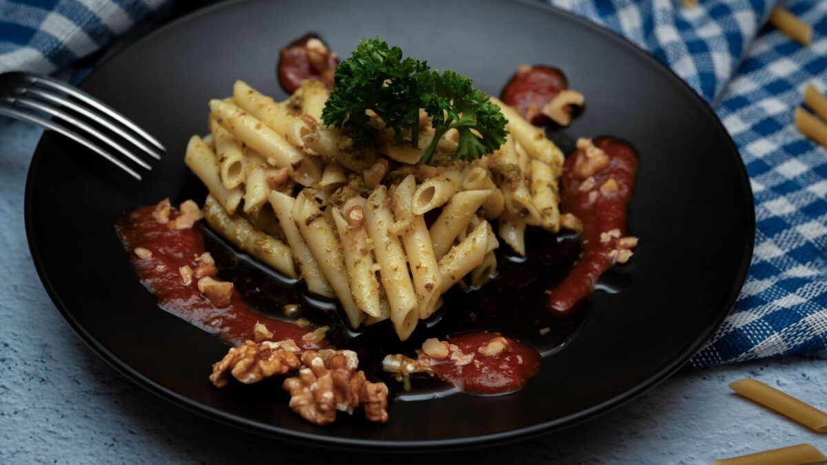 Penne pasta with walnuts and tomato sauce on a black plate, garnished with parsley.