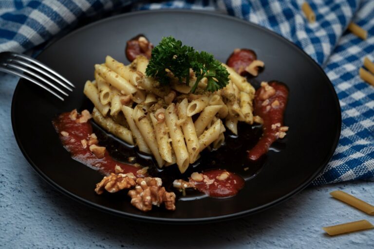 Penne pasta with walnuts and tomato sauce on a black plate, garnished with parsley.