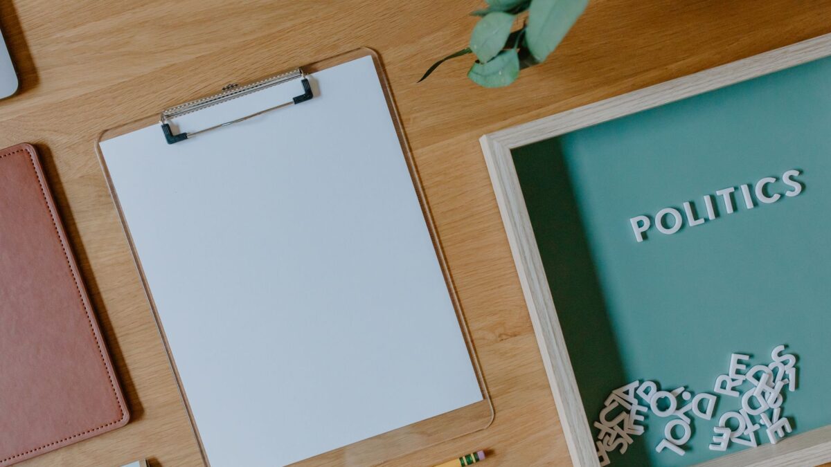Top view of a blank clipboard, scattered letters, and politics theme on a wooden desk.
