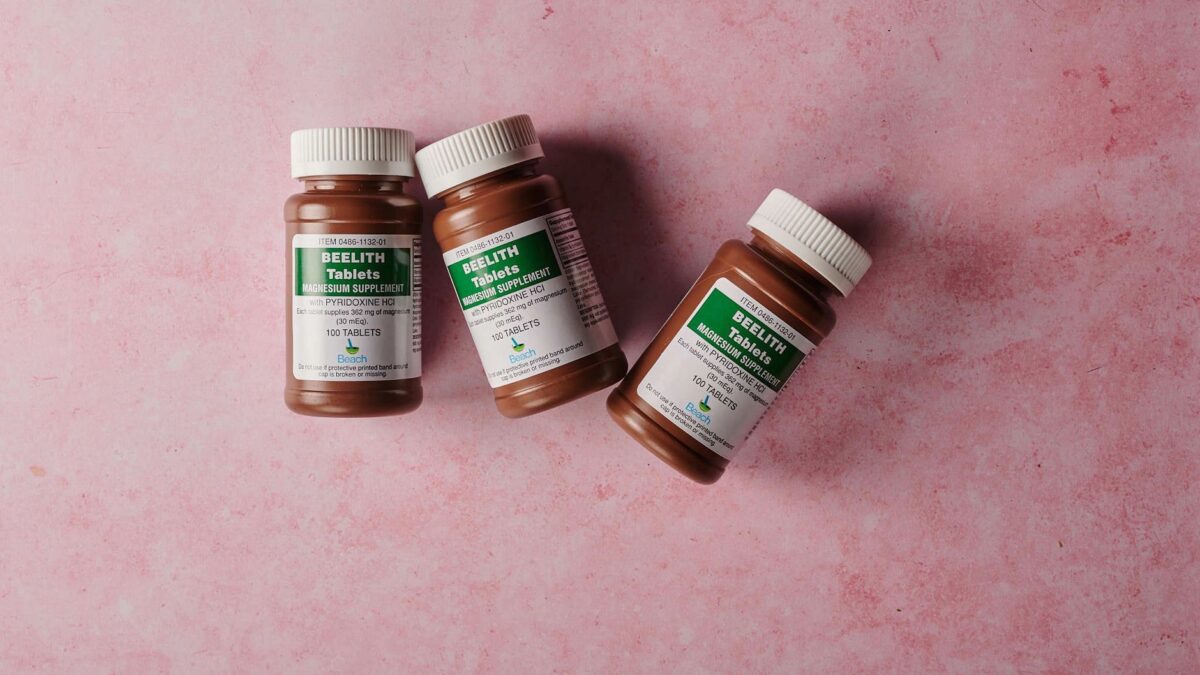 Three brown bottles of magnesium tablets on a soft pink background, ideal for health-themed content.