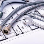 selfio - Close-up of plumbing tools and faucet on top of an architectural blueprint, perfect for har