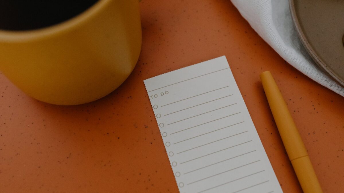 Notizblock mit handschriftlicher Checkliste, Kugelschreiber und Kaffeetasse auf einem Schreibtisch