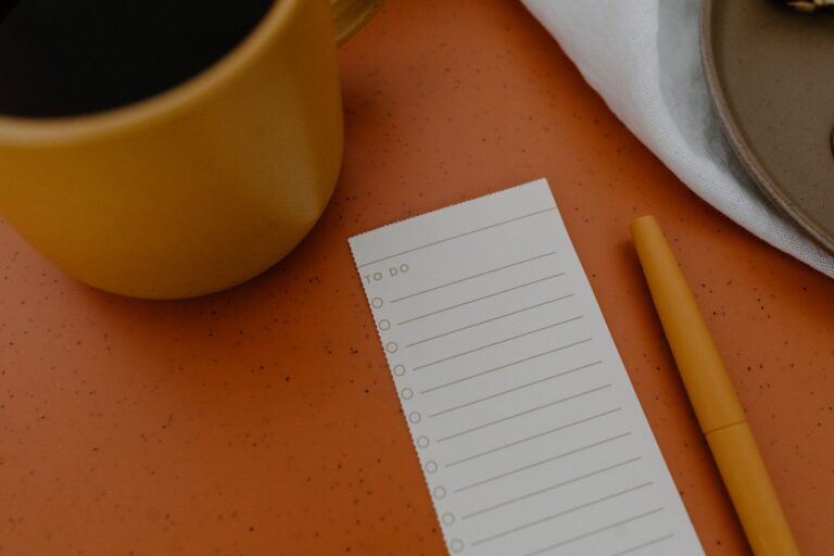 Notizblock mit handschriftlicher Checkliste, Kugelschreiber und Kaffeetasse auf einem Schreibtisch